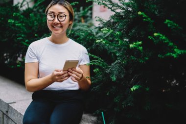 Şehirde boş zamanlarında cep telefonu kullanan neşeli Çinli kadın blogcu, gündelik giysiler içinde mutlu Japon hippi kız ve modern cep telefonu teknolojisini elinde tutan ve gülümseyen optik gözlük