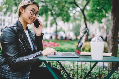 Optik gözlüklü mutlu kadın grafik tasarımcısı uzaktan kumanda sırasında web içeriğini tartışarak uluslararası olumlu bir konuşma yapıyor, dizüstü bilgisayarlı gülümseyen hippi kız