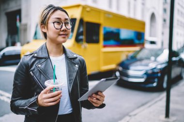 Seyahat sırasında dokunmatik ped kullanan gözlüklü kadın blogcu, gitmek için kahve tutan düşünceli Asyalı kız ve web sitesi paylaşımı için içerik yayınını düşünen dijital tablet