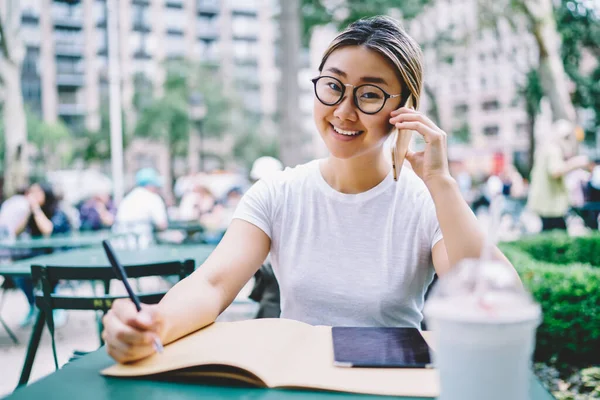 穿着眼镜的嬉皮士女孩在街头咖啡馆边学习边对着相机微笑 用国际手机交谈讨论教育信息 漫游连接的形象 — 图库照片