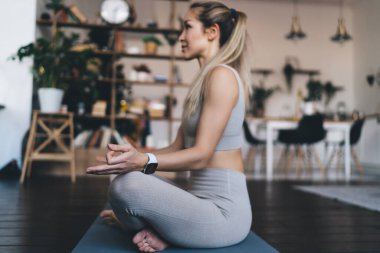 Avrupalı bir kız yoga zen pozu veriyor ve evde fitness minderi üzerinde meditasyon yapıyor. Sağlıklı yaşam tarzı kavramı. Spor giyim kuşamında kameraya bakarak gülümseyen güzel bir atletik kadın..