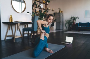 Avrupalı bir kız evde spor paspasının üzerinde geriniyor. Sağlıklı yaşam tarzı kavramı. Spor giyim ve yalınayak genç ve odaklanmış atletik kadın. Stüdyo dairenin içi.