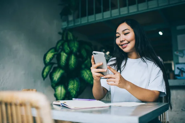 Uśmiechnięta Młoda Azjatycka Studentka Luźnym Stroju Czacie Smartfonie Siedząc Kawiarni — Zdjęcie stockowe