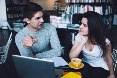 Yukarıdan gelen ciddi bir genç adam ve kadın kahve ve dizüstü bilgisayarla masaya oturup iş planının detaylarını tartışırken birbirlerine bakıyorlar.