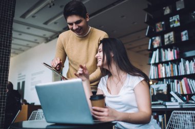 Modern kütüphanede dizüstü bilgisayarda çalışan güler yüzlü bayan meslektaşa dokümanları gösteren gündelik giysiler içinde neşeli genç bir adamdan.