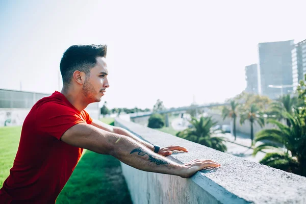 Spor elbiseli, spor elbiseli, koşuya hazırlanan, caddede taş duvara yaslanmış genç bir adamın yan görüntüsü.