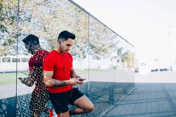 Spor giyim sektöründe beyaz bir adam cep telefonunda kablosuz 4g internet kullanarak spor bloguna bilgi paylaşmak için kardiyo alıştırmaları hakkında yayın yapıyor, kulaklıklı erkek koşucu dinlemek için medyayı seçiyor