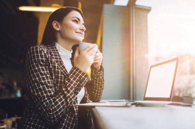 Düşük açılı, mutlu, zeki, serbest çalışan, sıcak bir şeyler içen ve kafeteryada dizüstü bilgisayarla yan yana oturan biri.