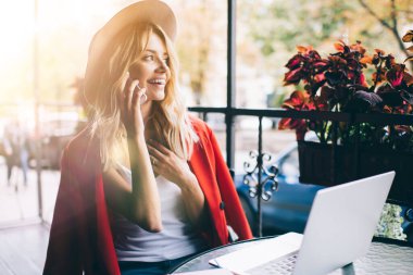 Neşeli bayan serbest çalışan, cep telefonuyla modern dizüstü bilgisayarlı neşeli moda blogcusu cep telefonu uygulaması aracılığıyla arayarak hafta sonu kafede dolaşırken arkadaşça mobil sohbetin keyfini çıkarıyor.