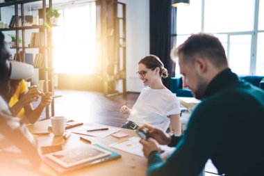 Bir grup farklı meslektaş masada oturup iş fikirlerini tartışırken akıllı telefonları karıştırıyor ve aydınlık odada kahve içiyor.