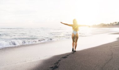 Sabahın erken saatlerinde ıslak kumlu plajda kolları açık beyaz mayo giyen ince kadın.