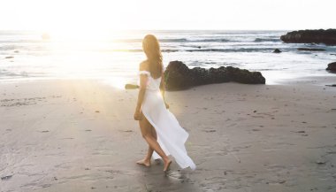 Yüzü olmayan, bronz tenli, beyaz elbiseli bir gezginin yaz tatilinde ıslak kumda tek başına yürümesi.