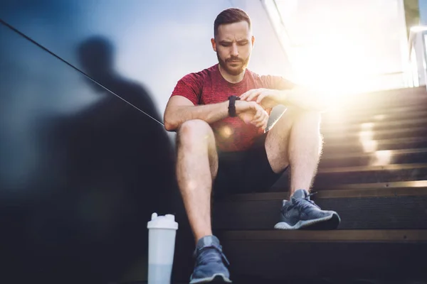 Niski Kąt Przemyślany Mężczyzna Trampkach Patrząc Smartwatch Wykonaniu Joggingu Ulicy — Zdjęcie stockowe
