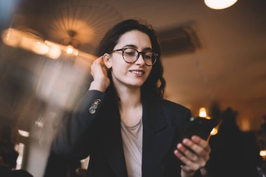 Resmi olarak gülümseyen kadın saçlarını düzeltirken cep telefonunu karıştırır ve kafede ekrana bakar.