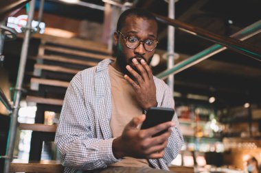 Modern cep telefonu okuma ile şok olmuş blog yazarı, dijital akıllı telefon teknolojisi olan siyahi hipster adam sosyal ağlarda cep telefonu sohbetleri sırasında etkilendi