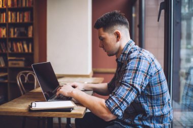 Beyaz tenli erkek öğrenci uzak mesafelere zaman harcıyor. Laptop uygulaması ile öğreniyor. Modern netbook 'ta 4G kablosuz bağlantı kuran yetenekli hipster çocuk, bilgilendirici web yayınlarını arıyor.