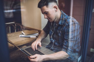Elektronik kulaklıklı beyaz bir adam netbook sırasında özel web sitesi seyrediyor ve 4G internete bağlı öğreniyor, milenyum bağımsız dinleyen modern dizüstü bilgisayardan sesli mesaj alıyor.