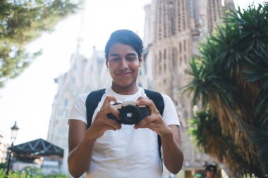 Kaygısız hipster gezintiden ve fotoğraf hobisinden zevk alan gezintide eski moda kamerayı test eden, Barcelona 'da gülümseyen klasik ekipmanlarda fotoğraf düzenleyen mutlu erkek fotoğrafçı.