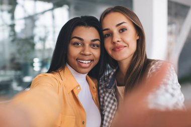 Cep telefonunda selfie çeken çok ırklı kız arkadaş portresi. Modern başarılı kadın kavramı. Arkadaşlık fikri. Kameraya bakan siyah ve Avrupalı genç kadınların seçici odak noktası