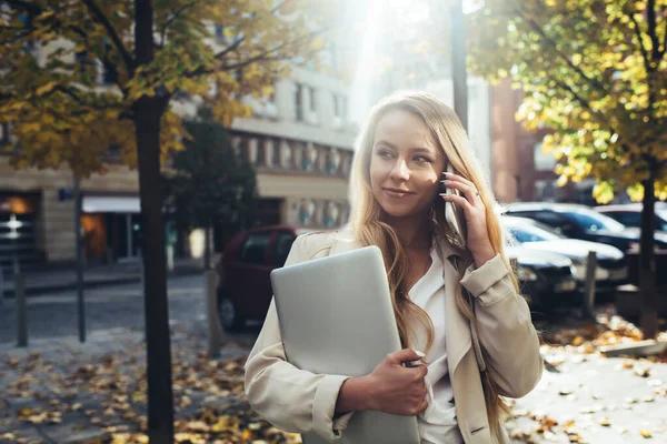 Сконцентрированная Восторженная Молодая Предпринимательница Элегантном Пальто Ноутбуком Разговаривает Телефону Прогуливаясь — стоковое фото