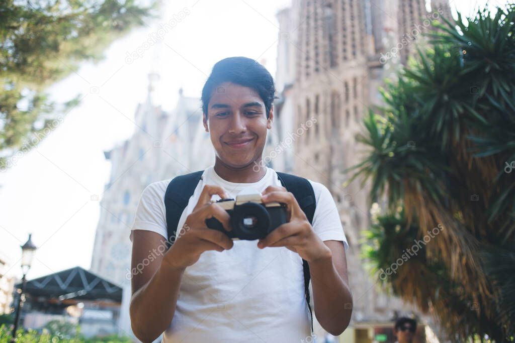 Carefree hipster guy enjoying travel vacations and time for photo hobby testing old fashioned camera during excursion,happy male photographer editing pictures at vintage equipment smiling in Barcelona