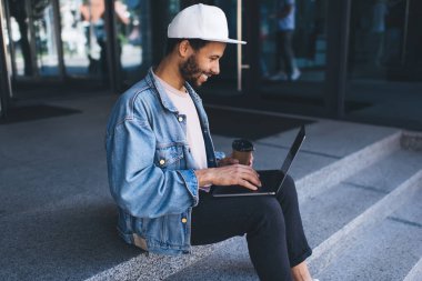 Kahveli mutlu bir erkek bilişim uzmanı. Şehir merdivenlerinde uzak mesafelere gidip serbest yaşam tarzının tadını çıkarıyor. Neşeli hipster, dizüstü bilgisayardan 4G 'ye bağlanan komik yayın haberleri okuyor.