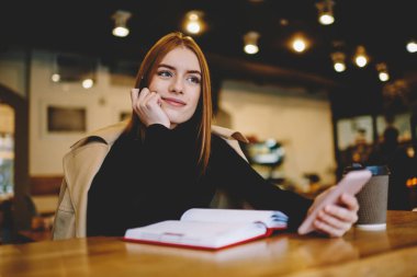 Moda kıyafetleri içinde düşünceli bir serbest yazar. Masada dizüstü bilgisayarla oturuyor ve rahat bir kafede proje üzerinde çalışırken akıllı telefonlara bakıyor.