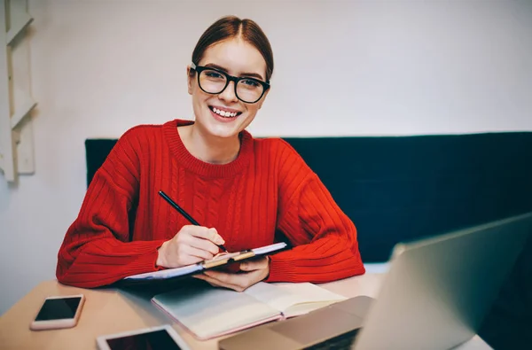 Mujer Sonriente Con Anteojos Suéter Punto Rojo Tomando Notas Mientras —  Fotos de Stock