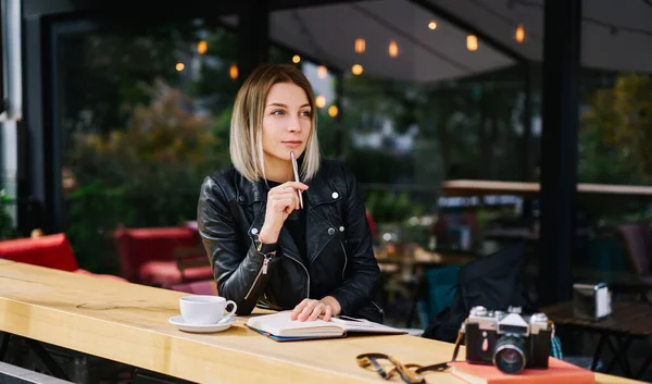 写真付きのテーブルでカフェに座っている若い女性とペンでノートを作って離れて見ている間に飲み物のカップ — ストック写真