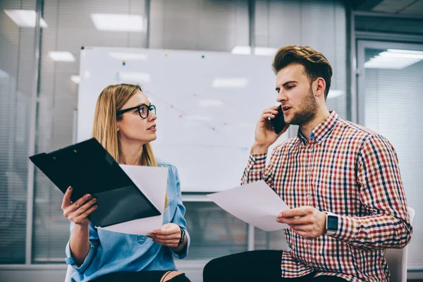 Modern konferans odasında oturan, iş stratejisi üzerinde çalışan ve arka planda beyaz tahtayla akıllı telefondan konuşan ciddi genç iş arkadaşları.