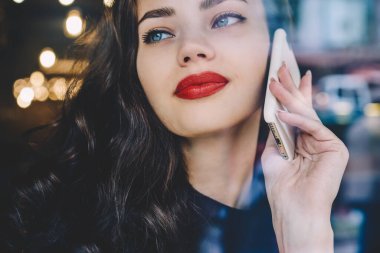 Uzun, kıvırcık saçlı, beyaz akıllı telefon kullanarak telefon eden, modern şehrin yansımasına bakan tarlacı kadın.