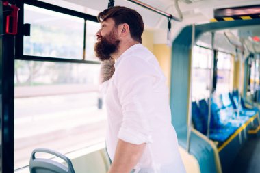 Gündüz vakti durmayı beklerken trende dikilip bakışlarını kaçıran sakallı genç bir adam.