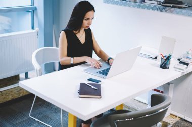 Modern ofis projesinde çalışırken siyah saçlı, dizüstü bilgisayarda yazan odaklanmış kadın girişimci.