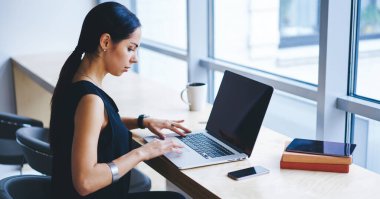 Çağdaş işyerindeki pencerenin yanındaki masada otururken iş için çalışan kadın uzaktan kumanda ağının yan görüntüsü