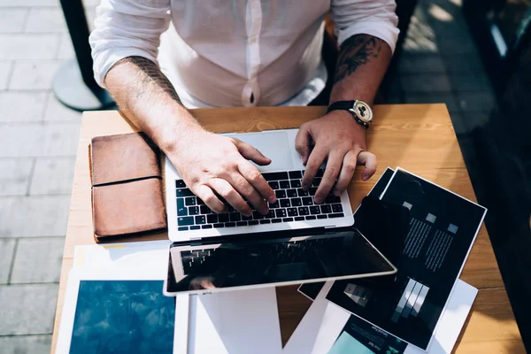 Uzaktan çalışma sırasında kağıt ve tabletle masada otururken netbook 'ta yazan isimsiz bir erkek çalışanın üstünden.