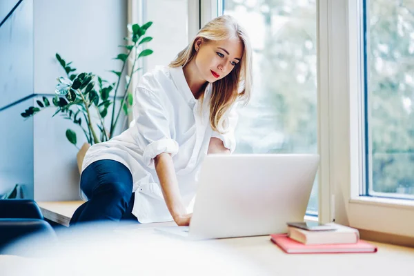 Konzentrierte Junge Frau Freizeitkleidung Sitzt Mit Laptop Auf Der Fensterbank — Stockfoto