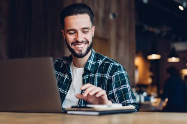 Neşeli beyaz adam internet projesi yaparken gülümsüyor. Laptop teknolojisini kullanarak birlikte çalışıyor, başarılı bir milenyum çalışanı. 20 yaşında, modern netbook bilgisayarıyla masa başına gülüyor.