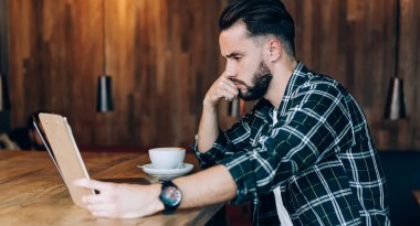 Mutsuz erkek öğrenci sınav hazırlıkları ve birlikte çalışma alanında öğrenme süresince şaşkın hissediyor, kafası karışık metin yazarı bilgisayarla çalışırken notları kontrol ediyor.