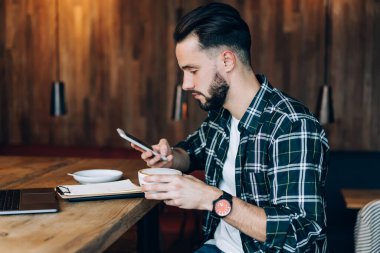 Çevrimiçi mesajlaşma ve sosyal medya için modern cep telefonu aygıtı kullanan Kafkasyalı erkek öğrencinin yan görüntüsü, akıllı telefon bildirimini kontrol eden yetenekli blogcu