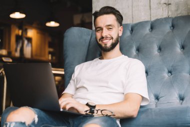 Kameraya gülümseyen yetenekli hipster adamın portresi birlikte çalışma alanında dizüstü bilgisayar işi yaparken modern netbook teknolojisiyle eğlenen neşeli bir erkek blog yazarı.