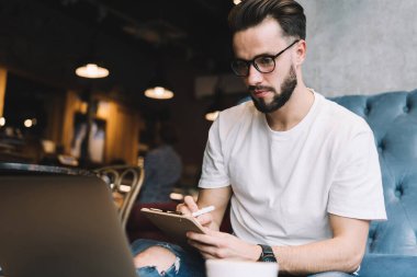 Beyaz tenli erkek öğrenci optik göz giysisinde dizüstü bilgisayar başında webinar videolar izliyor ve birlikte çalışma alanında öğrenim görüyor. Yetenekli adam netbook aracılığıyla eğitim sırasında bilgi verici yayınları arıyor.