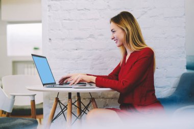 Cafe 'de çalışırken şık giyinmiş, laptopta oturup yazı yazan neşeli bir kadın.