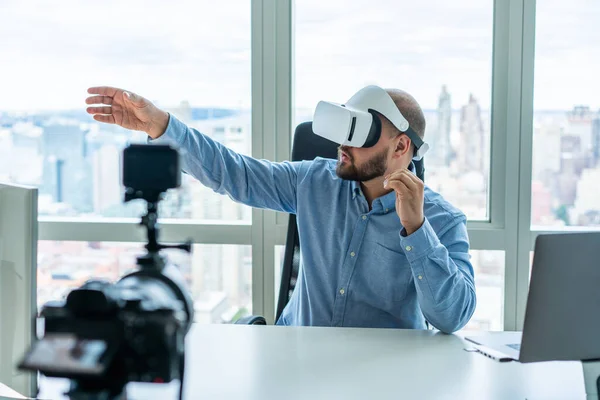 現代のオフィスでは サイバー空間を体験しながら 仮想現実のヘッドセットを身に着けている集中髭の男と三脚にカメラでビデオを記録 — ストック写真