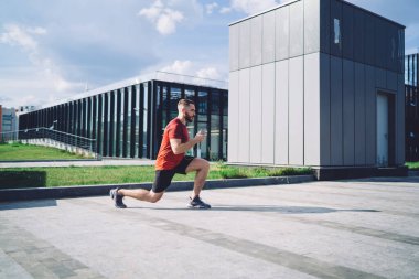Sabahları ısınırken sokakta esneme egzersizi yapan ve kulaklıkla müzik dinleyen ve gözlerini kaçıran tüm vücudun yan görüntüsü.