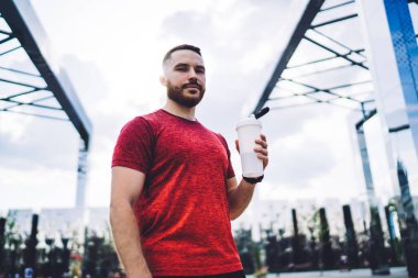 Koşarken ve kameraya bakarken elinde plastik bir şişe su tutan yakışıklı sakallı sporcudan.