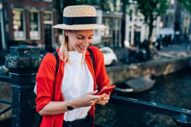 Neşeli bayan gezgin, Amsterdam 'da yolculuk yaparken köprünün korkuluklarına yaslanırken cep telefonunu karıştırıyor.