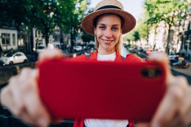 Eski şehri keşfeden neşeli bir kadın ve Amsterdam 'da tatillerde köprüden karşıya geçerken modern cep telefonuyla selfie çekiyor.