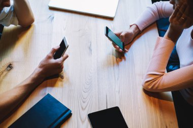 Yukarıdan gelen isimsiz öğrencilerin günlük kıyafetlerini giyip ahşap masada oturarak akıllı telefonları karıştırarak projenin detaylarını tartışıyorlar.