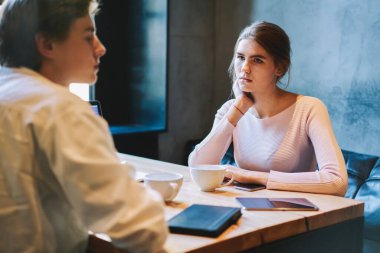 Genç, ciddi bir bayan, gündüz kafede oturmuş erkek arkadaşını izliyor ve bir fincan içki içiyor ve masada tabletle günlük giysiler giyiyor.