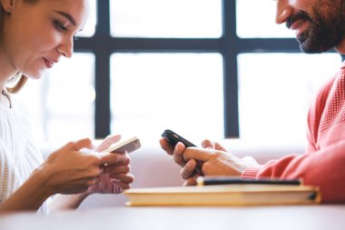 Kafede otururken akıllı telefondan mesajlaşan, günlük kıyafetli yetişkin bir adamın cep telefonu kullanışının yan görüntüsü.